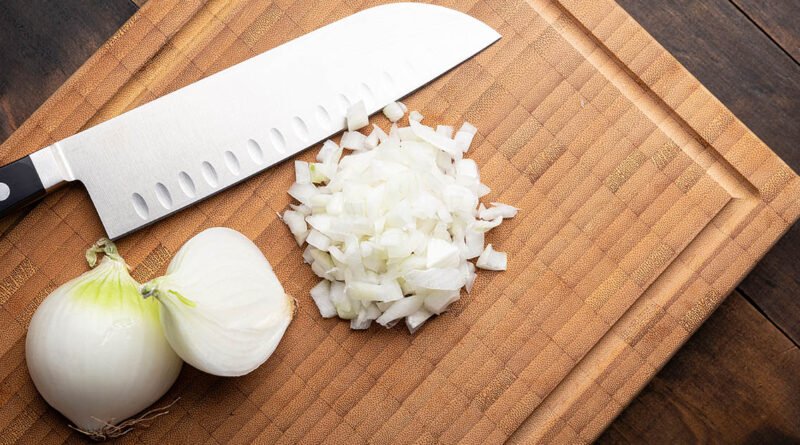 Cebolla blanca fresca picada sobre tabla de cortar de madera