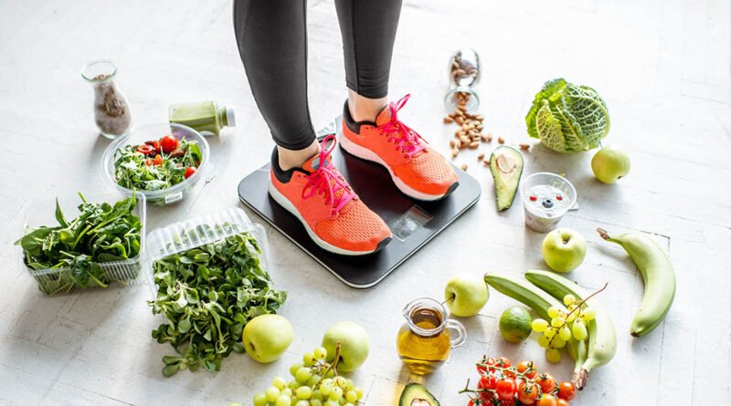 Mujer sobre balanza rodeada de alimentos saludables