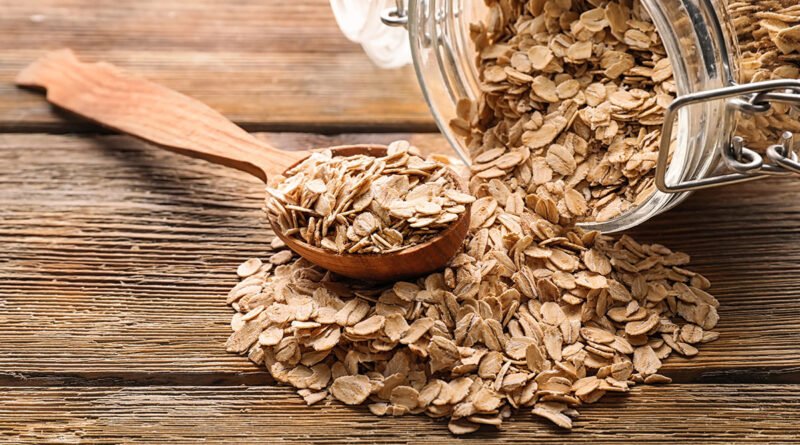 Frasco de vidrio y cuchara con copos de avena sobre una mesa de madera