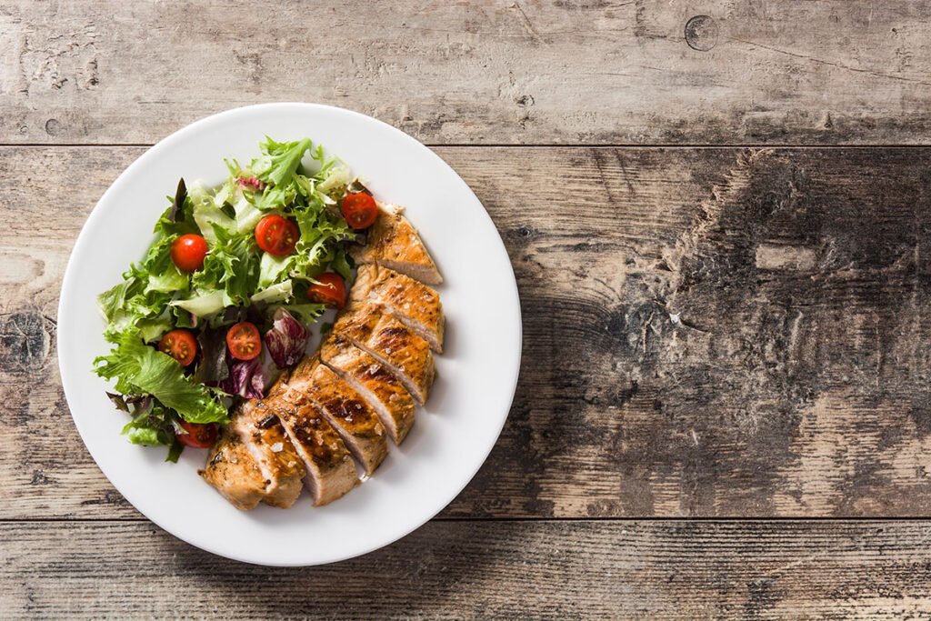 Plato con pechuga de pollo grillada y verduras sobre una mesa de madera