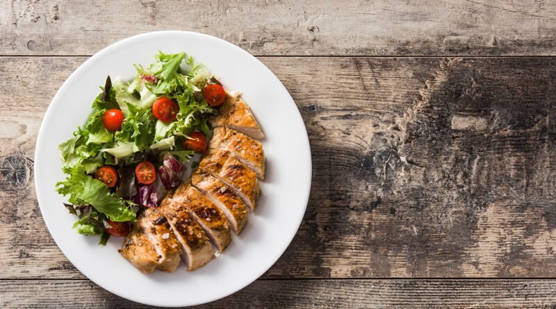 Plato con pechuga de pollo grillada y verduras sobre una mesa de madera