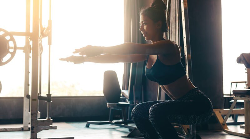 Mujer con ropa deportiva haciendo una sentadilla en el gimnasio